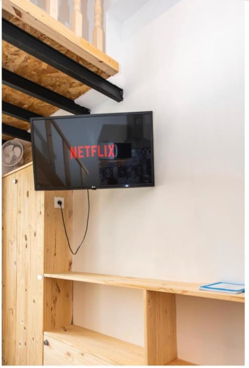 Téléviseur mural affichant le logo Netflix au-dessus d'un bureau en bois et d'étagères dans la chambre studio de la Villa des Palmiers