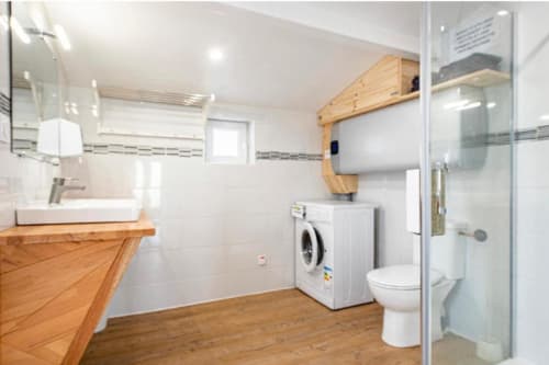 Salle de bain moderne à la Villa des Palmiers avec meuble-lavabo en bois, machine à laver, toilettes et douche à l'italienne