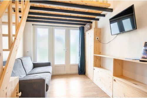 Studio moderne à Villa des Palmiers avec poutres apparentes, canapé gris, étagères en bois, télévision écran plat et portes vitrées