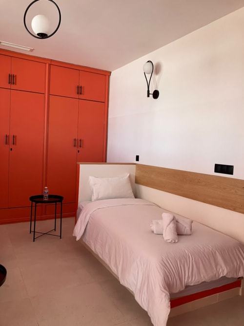 Modern bedroom at SAMYAflat Tangier with red wardrobes, pink bedding, wooden headboard, and contemporary wall sconces