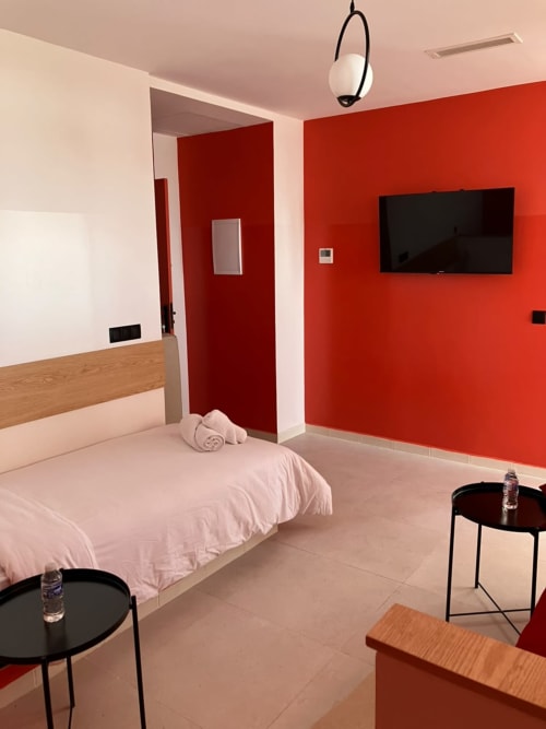 Modern apartment bedroom at SAMYAflat Tanger with red accent wall, flat-screen TV, pink bedding, and contemporary furnishings