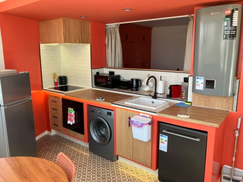 Modern kitchen in YaYaCaSa Ocre apartment at SAMYAflat, Tangier, with red walls, wood cabinets, and stainless steel