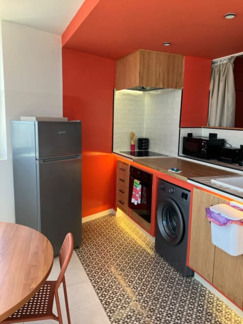Modern kitchen with vibrant red walls, wood cabinets, black appliances, and washing machine in YaYaCaSa Ocre apartment at
