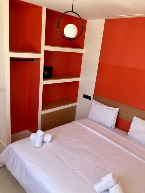 Modern bedroom at SAMYAflat in Tangier with red accent walls, wooden bed, white bedding, and built-in red shelving