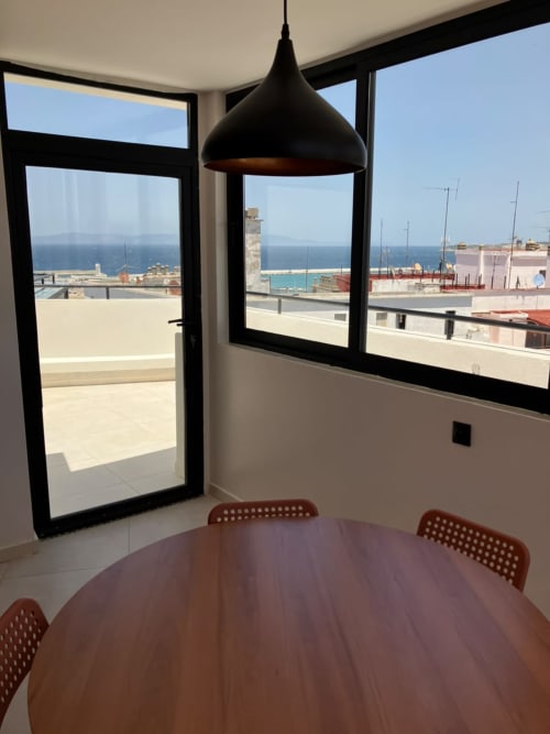 Modern dining area with sea view in Tangier apartment, featuring round table and pendant lamp overlooking coastline