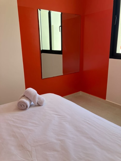 Minimalist bedroom with white bed, rolled towels, and bold red accent wall with window at SAMYAflat Tanger apartment