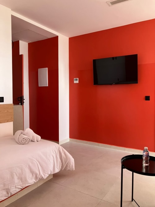 Modern bedroom at SAMYAflat in Tangier with bold red accent wall, flat-screen TV, white bed, and minimalist furnishings