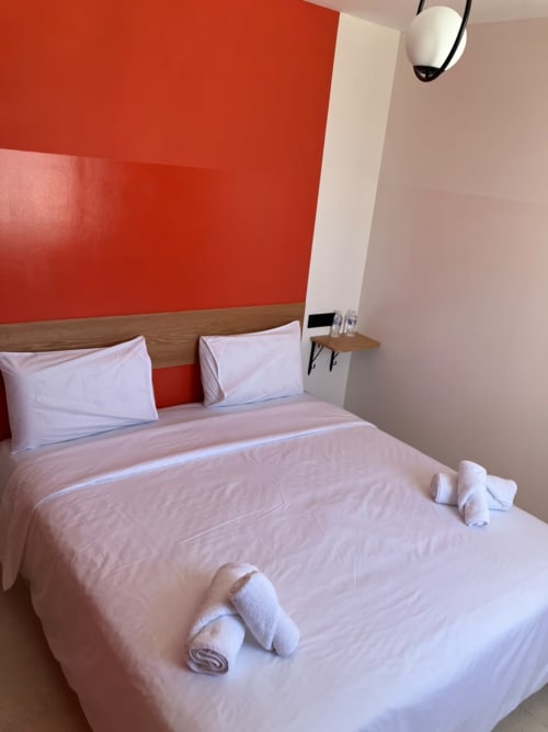 Modern hotel bedroom at SAMYAflat in Tangier with red accent wall, wooden bed frame, white linens, and rolled towels