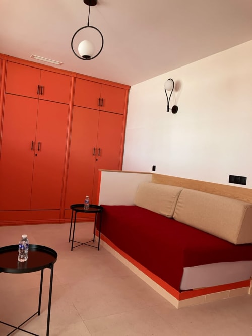 Modern bedroom at SAMYAflat in Tangier with red wardrobe, beige bed, black pendant light and side tables