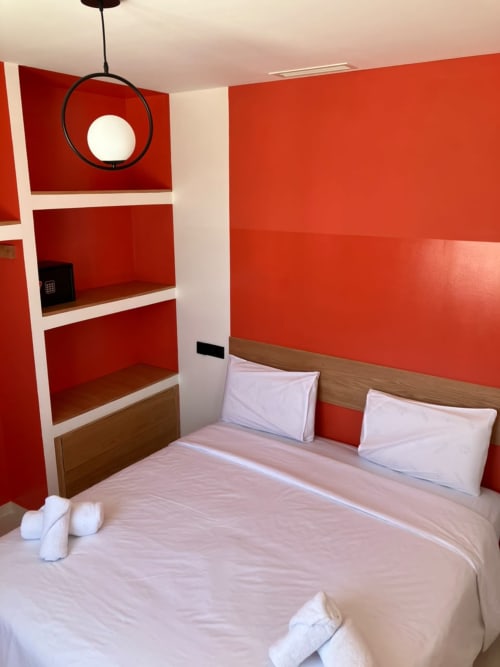 Modern bedroom at SAMYAflat in Tangier with vibrant red walls, wooden bed frame, white bedding, shelving unit, and pendant