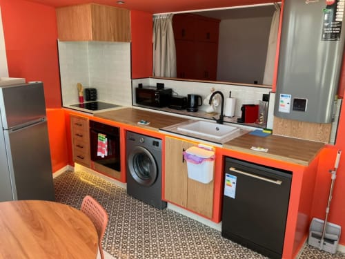 Modern kitchen with vibrant orange cabinetry, stainless steel appliances, and wood countertops at SAMYAflat apartment in