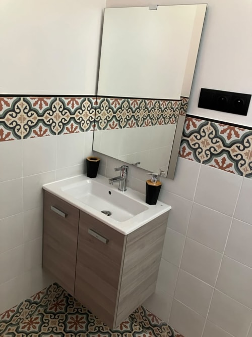 Modern bathroom vanity with white sink, wooden cabinet, decorative Moroccan tile border, and mirror at SAMYAflat in Tangier