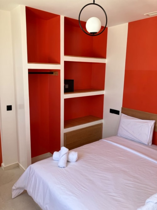 Modern bedroom at SAMYAflat in Tangier with red shelving unit, white bedding, and contemporary pendant light fixture