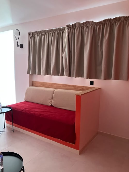 Modern red sofa bed with beige pillows in SAMYAflat apartment, Tangier, featuring taupe curtains and wood headboard