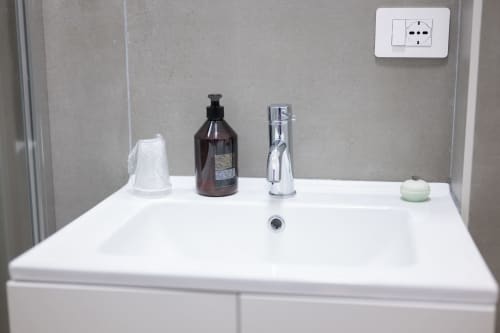 Lavabo moderno con rubinetto cromato, dispenser sapone marrone e tazza bianca nell'appartamento Newhouse, Modugno Italia