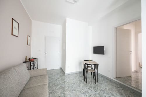 Moderno soggiorno in Modugno con divano grigio, TV schermo piatto, tavolo da pranzo e pareti bianche minimaliste
