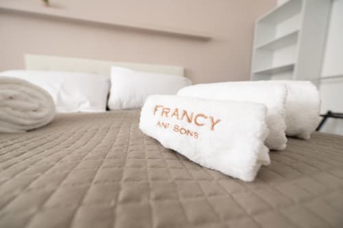 Asciugamani bianchi arrotolati con marchio Francy and Sons sul letto dell'appartamento Newhouse a Modugno, Italia