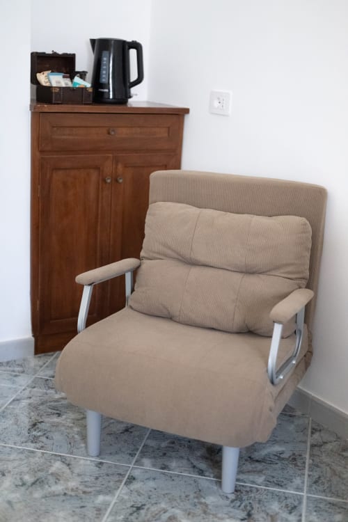 Poltrona beige con cuscini nella camera Francy 3 dell'hotel Newhouse di Bari, con credenza in legno e bollitore