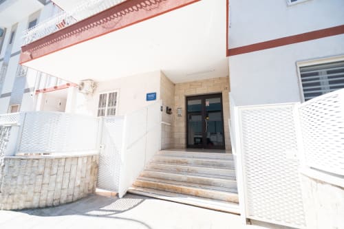 Ingresso dell'hotel Newhouse a Bari con cancellata bianca, scalinata piastrellata e porta scura che conduce alla camera Francy 3