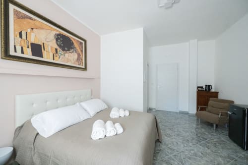 Camera moderna all'hotel Newhouse di Bari con letto queen, biancheria bianca, parete rosa, opere d'arte e vista sulla città