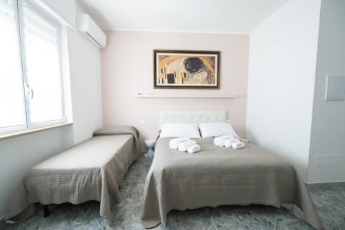 Camera doppia luminosa dell'hotel Newhouse a Bari con pareti rosa, due letti, cuscini bianchi, finestra e opere d'arte