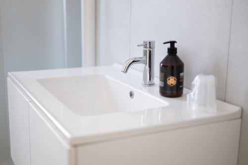 Lavabo bianco moderno con rubinetto cromato e dispenser di sapone scuro presso l'hotel Newhouse di Bari