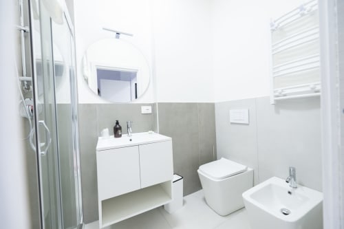 Bagno moderno dell'hotel Newhouse a Bari con lavabo bianco, toilet, bidet, specchio rotondo e zona doccia