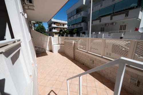 Terrazza soleggiata dell'hotel Newhouse a Bari con pavimentazione in piastrelle, ringhiere forate e vista sui vicini edifici