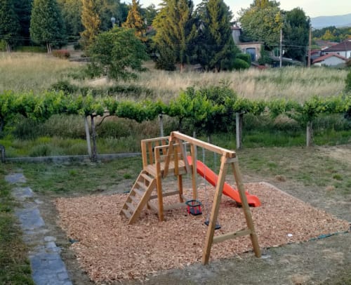Wooden playground with red slide at Vacationgalicia in Pantón, Lugo, surrounded by vineyard landscape.
