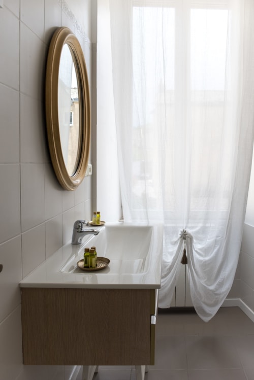 Salle de bains moderne avec plan de travail blanc, miroir encadré de laiton et rideaux blancs à La Demeure du Comte