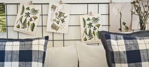 Dormitorio de apartamento de arte en Barcelona con almohadas a cuadros, láminas botánicas en pared rejilla y flores secas como decoración