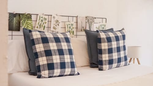 Acogedora habitación de apartamento barcelonés con almohadas de cuadros, ropa de cama neutra y arte botánico en la pared sobre la cama