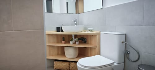 Baño moderno en apartamento de Barcelona con tocador de madera, lavabo blanco tipo recipiente, inodoro y estanterías abiertas con decoración
