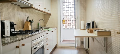 Cocina moderna en apartamento de Barcelona con muebles blancos, encimeras de granito, estufa a gas y pequeña zona de comedor con azulejos