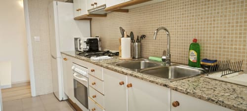 Cocina moderna en apartamento de Barcelona con encimera de granito, armarios blancos, fregadero de acero inoxidable y vitrocerámica