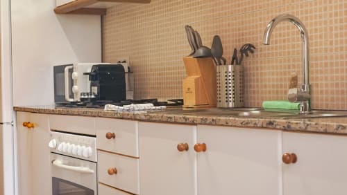 Cocina moderna en apartamento de Barcelona con muebles color crema, encimera de mármol, fregadero de acero inoxidable y elementos esenciales de cocina