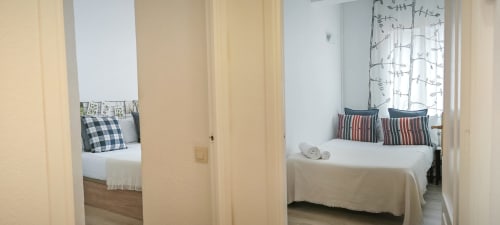 Dos luminosos dormitorios en BCNMADflats Barcelona con ropa de cama blanca, almohadas rayadas y puertas abiertas mostrando diseño moderno