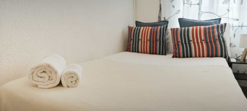 Acogedor dormitorio en el apartamento Barcelona Art de BCNMADflats con toallas enrolladas en cama blanca y almohadas a rayas.