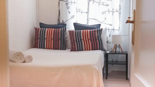 Dormitorio moderno en BCNMADflats Barcelona con almohadas rojas y negras, ropa de cama blanca y arte botánico en la pared