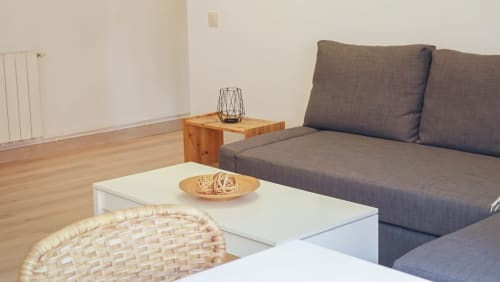 Sala de estar de apartamento moderno en Barcelona con sofá gris, mesa de café blanca, mesa auxiliar de madera y puffs de mimbre