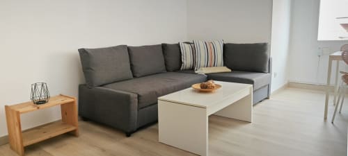Salón moderno en apartamento de Barcelona con sofá gris oscuro en esquina, mesa de café blanca y mesita de madera
