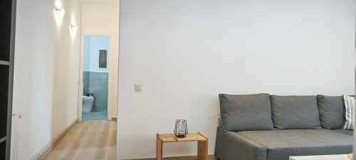 Sala de estar de apartamento moderno en Barcelona con sofá gris, mesita de madera y pasillo hacia el baño