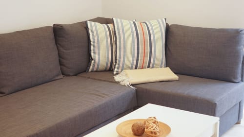Sofá de esquina gris con cojines a rayas y manta en sala de estar de apartamento en Barcelona