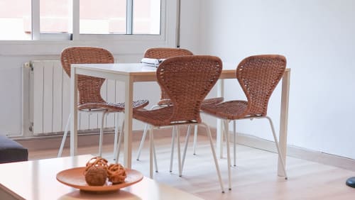 Comedor moderno en apartamento de Barcelona con sillas de ratán, mesa de madera y luz natural desde las ventanas