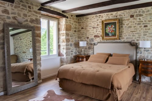 Chambre La Comtesse à La Demeure du Comte avec murs en pierre, literie beige, poutres en bois et vue sur le jardin
