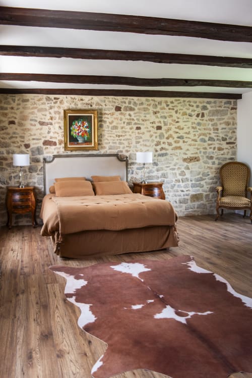 Chambre La Comtesse à La Demeure du Comte : murs en pierre, plafond à poutres, literie beige et tapis en peau de vache