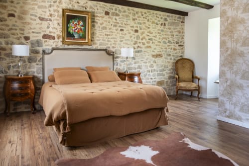 Chambre élégante à La Demeure du Comte avec murs en pierre, lit queen-size en lin beige et vue sur le jardin à Marcillac-Vallon