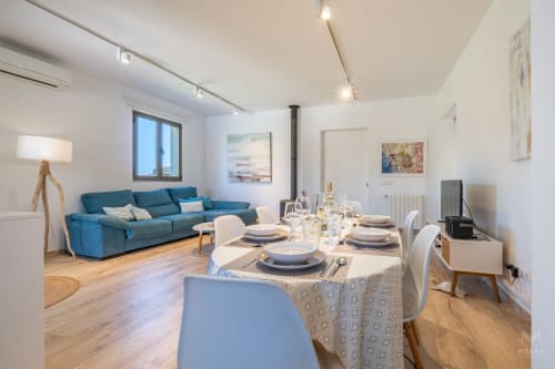 Villa moderna con sala de estar y comedor, sofá azul, mesa puesta y suelos de madera en Artà