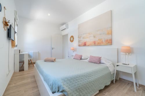 Dormitorio moderno en villa Can Colomer Ferragut en Artà con cama, almohadas rosas, mesita blanca y obras de arte