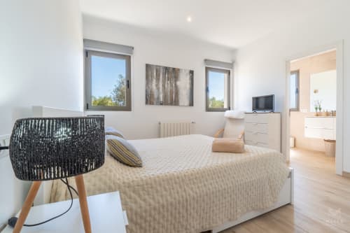 Dormitorio de villa moderna en Artà con vistas a la montaña, ventanales luminosos, mobiliario contemporáneo y baño en suite